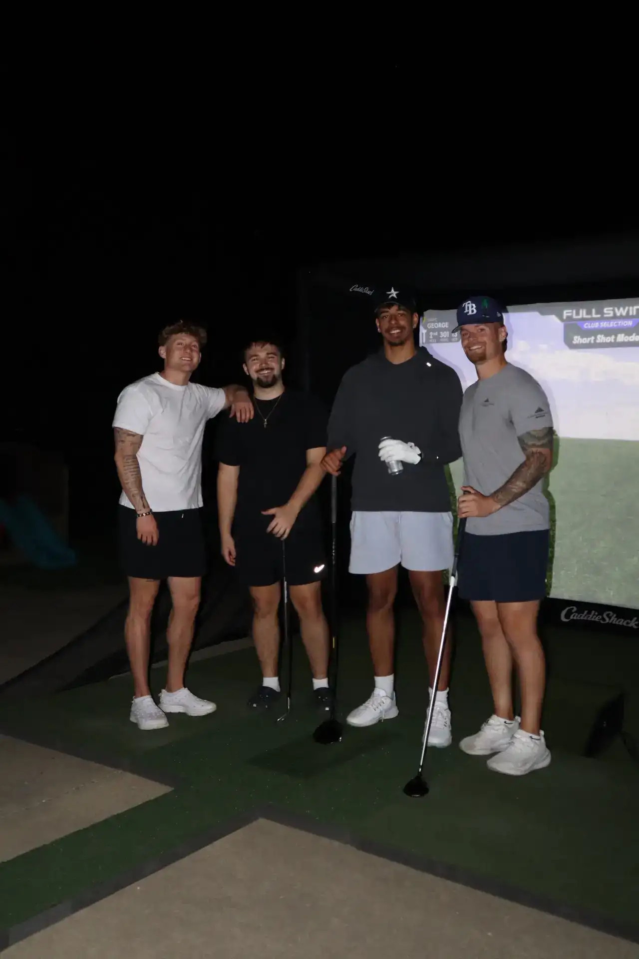 Four friends with golf clubs posing at a CaddieShack portable golf simulator setup