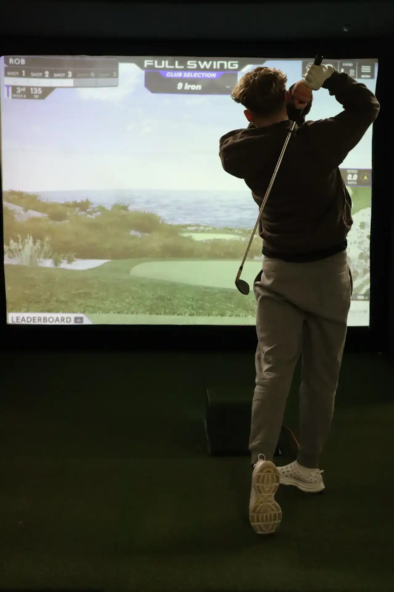 Golfer finishing a 9 iron swing on a Full Swing golf simulator screen