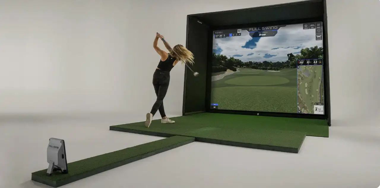 Golfer swinging a driver into a Full Swing golf simulator with hitting mat and launch monitor