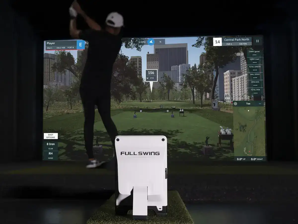Golfer mid-swing on a Full Swing golf simulator displaying shot data on screen